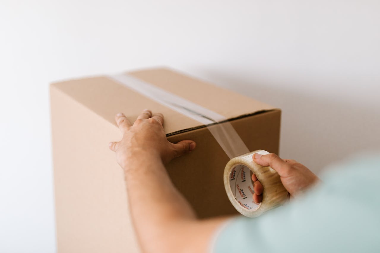 Crafting Captivating Headlines: Your awesome post title goes here Hands sealing a cardboard box with tape, prepping for a move or delivery indoors.